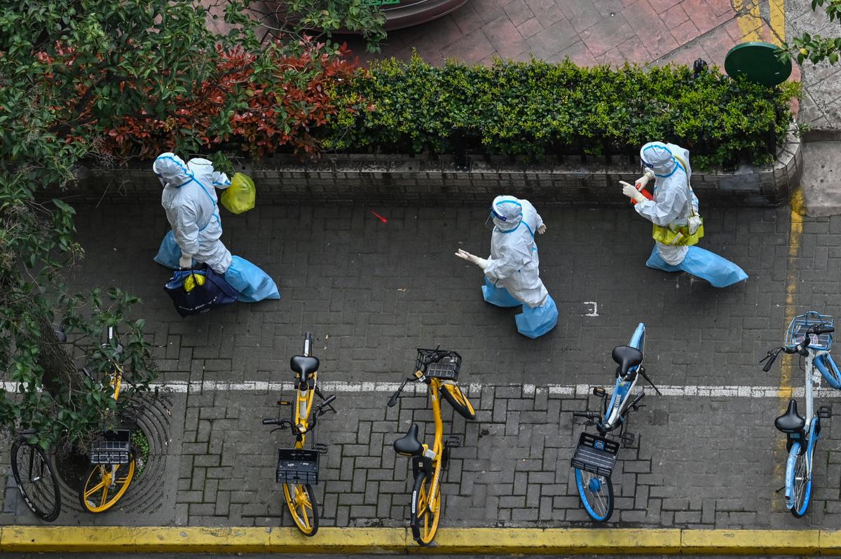 Health workers wearing personal protective gear walk next to a residential compound during the second stage of a Covid-19 lockdown in Jing'an district in Shanghai on April 1, 2022. (Hector Retamal/AFP via Getty Images)