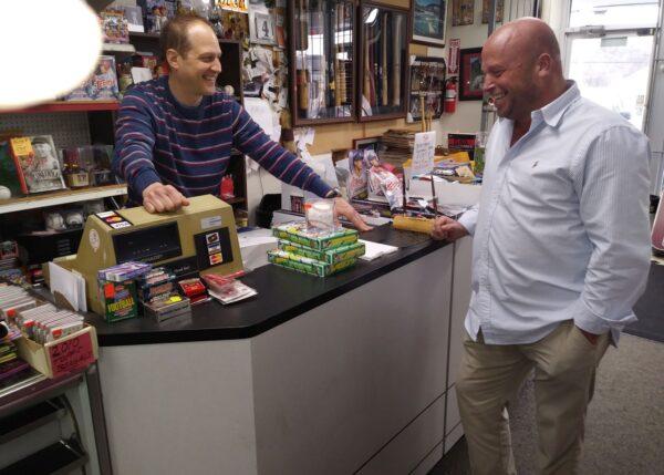 Mike Siska of Ideal Baseball Cards in Cincinnati (L) and customer Steve Denier (R) share some good times in the shop, which specializes in new and vintage sports cards. Siska said collectors still like to purchase packs of the new Topps cards every year, but after Fanatics purchased the Topps Co. in January, Siska said he believes changes will come to the hobby. (Michael Sakal/The Epoch Times)