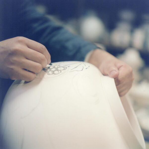 Japanese ceramicist Imaemon Imaizumi XIV draws a design on a piece of porcelain. Imaemon is the 14th generation of his family to inherit the secret to his family’s traditional overglaze. “Imaemon Imaizumi XIV, from 'The Ateliers of Wonders Series, 2020,'” by photographer Rinko Kawauchi. (Rinko Kawauchi/Michelangelo Foundation)