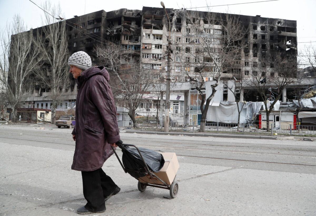 An elderly woman crosses a street near a building damaged in the course of Ukraine-Russia conflict in the southern port city of Mariupol, Ukraine, on April 1, 2022. (Alexander Ermochenko/Ukraine)