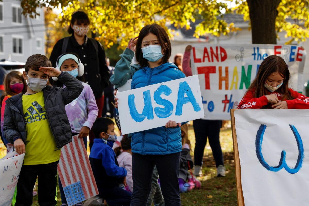 Children wearing masks stand holding signs during a Veterans Day ceremony at the John Philip Sousa Memorial Bandshell at Sunset Park in Port Washington, N.Y., on Nov. 11, 2021. (Shannon Stapleton/Reuters)