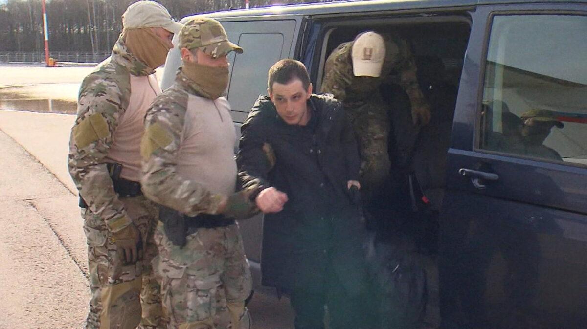 Former U.S. Marine Trevor Reed, who was detained in 2019 and accused of assaulting police officers, is escorted to a plane in Moscow, Russia, by Russian service members as part of a prisoner swap between the U.S. and Russia, in this still image taken from video released April 27, 2022. (RU24/Handout via Reuters TV)