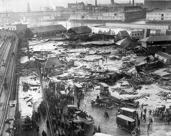 A panorama of the Great Molasses Flood site. Wreckage of the collapsed tank is visible in the background and center, next to a light-colored warehouse. An elevated railway structure is visible at far left. (Commons.Wikimedia / Public Domain)