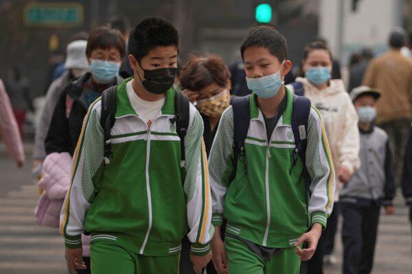 Students and residents wearing protective masks walk across a street in Beijing on April 11, 2022. (Andy Wong/AP Photo)