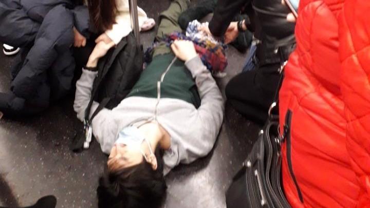 People tend to a bloodied passenger lying on the subway floor at the 36th Street station in Brooklyn, New York, on April 12, 2022. (Epoch Times staff)