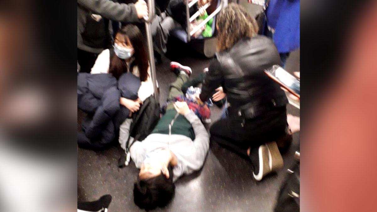 People tend to a bloodied passenger lying on the subway floor after a shooting at the 36th Street station in Brooklyn, N.Y., on April 12, 2022. (Epoch Times staff)