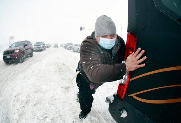 Matt Mittelstaedt, a driver for Missouri Slope Lutheran Care Center, pushes as a Good Samaritan tows the large passenger van he was driving when it got stuck in the snow at the intersection of State Street and Divide in Bismarck, N.D., on April 12, 2022. (Mike McCleary/The Bismarck Tribune via AP)