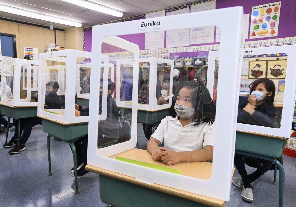 Children wearing masks sit behind screened-in cubicles as they learn in their classroom after getting their pictures taken at picture day at St. Barnabas Catholic School during the COVID-19 pandemic in Scarborough, Ont., on Oct. 27, 2020. (The Canadian Press/Nathan Denette)