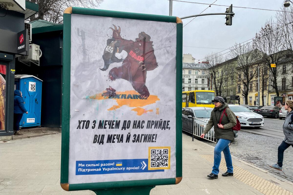 A poster depicts a Russian bear standing on top of the shape of Ukraine with one leg bitten off by a honey badger, which is now attacking the bear's arm. The badger wears a vest marked with the acronym for the Ukrainian armed forces. "Those who come to us with a sword, on the sword will die," the poster reads. (Charlotte Cuthbertson/The Epoch Times)