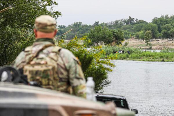  A Texas National Guardsman watches as a group of Cubans cross the Rio Grande from Mexico toward the United States in Eagle Pass, Texas, on April 19, 2022. (Charlotte Cuthbertson/The Epoch Times)