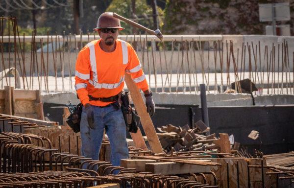 A worker tosses a hammer to a colleague as freeway construction continues on the State Route 73 southern interchange from the Interstate 405 in Costa Mesa, Calif., on April 21, 2022. (John Fredricks/The Epoch Times)