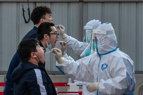 Health workers dressed in protective clothing give nucleic acid tests to men at a mass testing site to prevent COVID-19 on March 14, 2022 in Beijing, China. (Photo by Kevin Frayer/Getty Images)