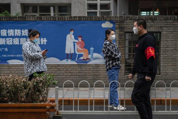 People wait in line for nucleic acid tests to detect COVID-19 next to a poster for vaccinations at a makeshift testing site in the Central Business District in Chaoyang in Beijing, China on April 27, 2022. (Kevin Frayer/Getty Images)