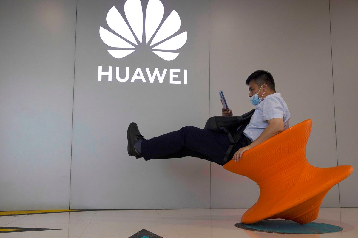 A man wearing a protective face mask sits near a Huawei store logo in Beijing on July 31, 2020. (Ng Han Guan/AP Photo)