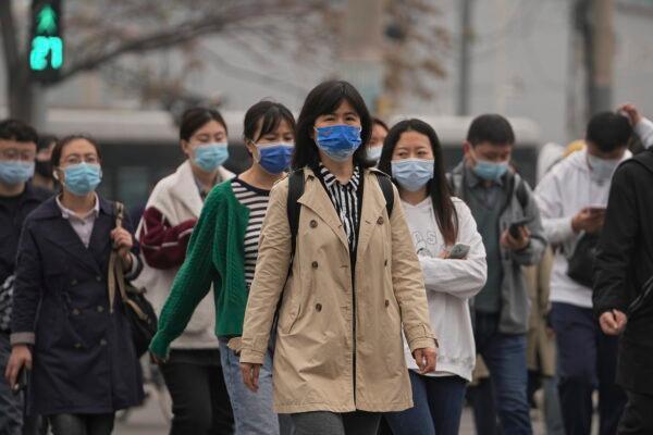 People wearing protective masks walk across a street in Beijing during the morning rush hour on April 11, 2022. (Andy Wong/AP Photo)