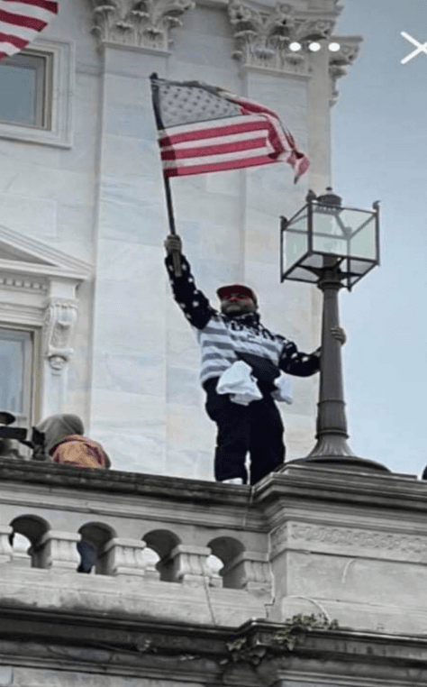 A screenshot of an image from Kash Kelly's cell phone shows him standing on the ledge of the staircase at the Capitol on Jan. 6, 2021, waving an American Flag. (U.S. District Court for the District of Columbia)