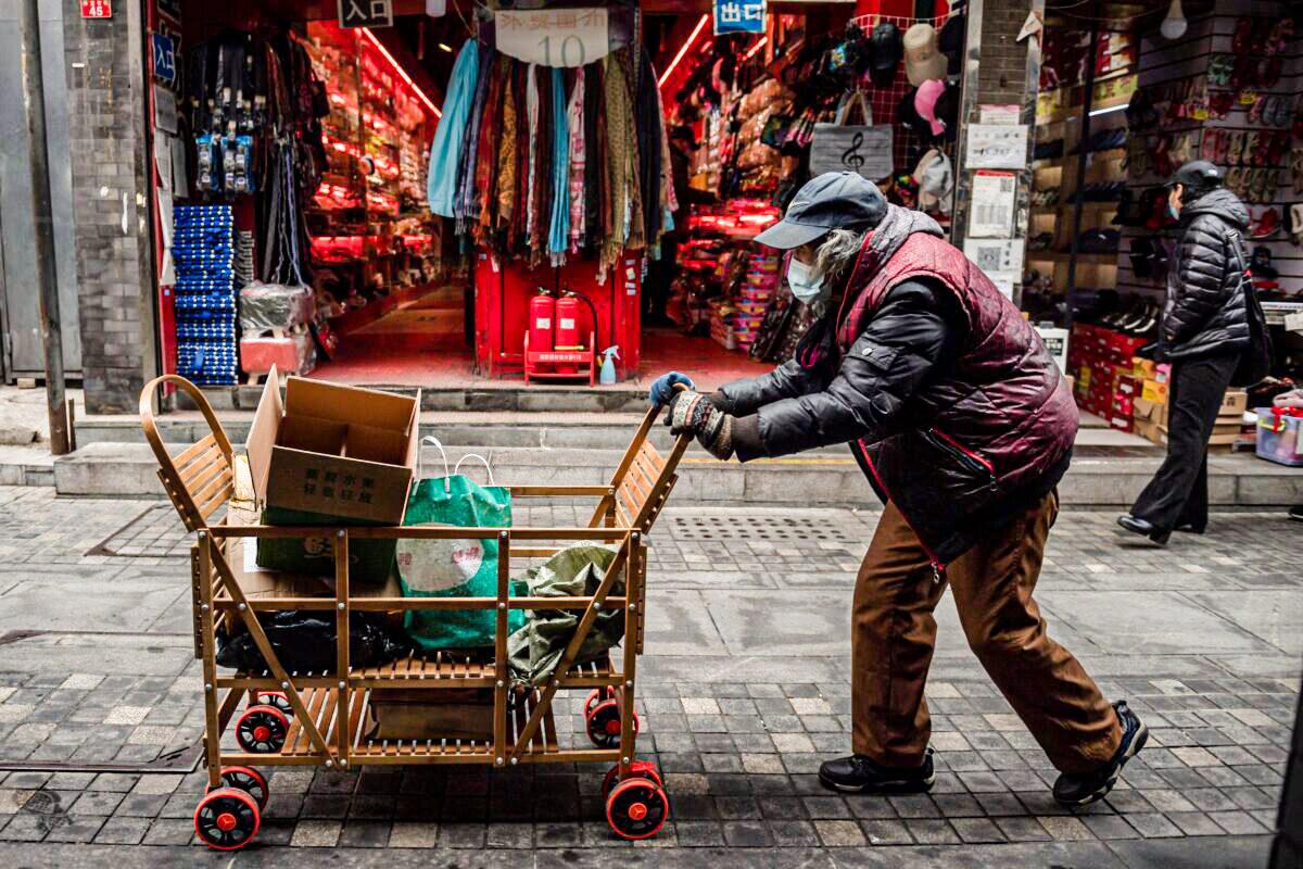 An elderly woman pushes a cart after searching through garbage bins to collect recyclable items to sell along a street near the Great Hall of the People in Beijing on March 5, 2021. (Nicolas Asfouri/AFP via Getty Images)