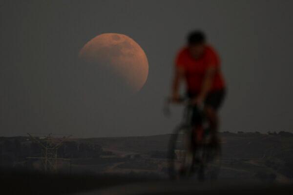 A lunar eclipse behind a cyclist during the first blood moon of the year, in Irwindale, Calif., on May 15, 2022. (Ringo H.W. Chiu/AP Photo)