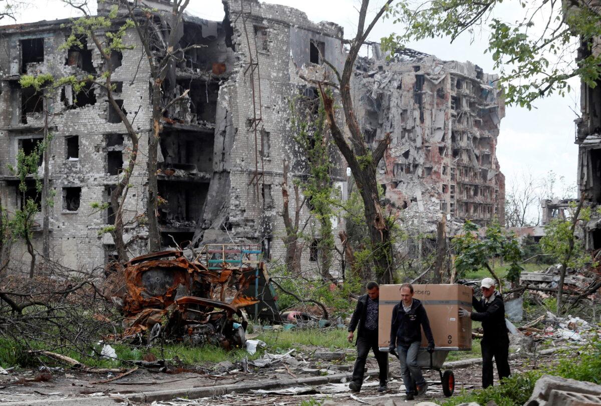 Residents transport a box on a wheelbarrow past a heavily damaged apartment building near Azovstal Iron and Steel Works during the Ukraine-Russia conflict in the southern port city of Mariupol, Ukraine, May 22, 2022. (Alexander/Reuters)