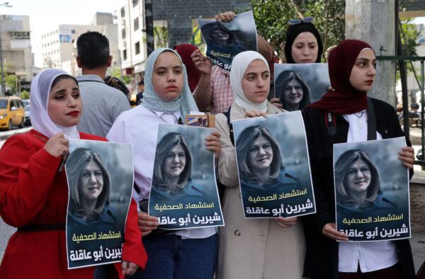  Palestinians hold posters displaying veteran Al Jazeera journalist Shireen Abu Akleh, who was fatally shot as she covered a raid on the West Bank's Jenin refugee camp in the West Bank city of Hebron, on May 11, 2022. (Hazem Bader/AFP via Getty Images)