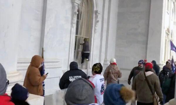 Police converge on Hunter Ehmke as he punches out a window at the U.S. Capitol on Jan. 6, 2021. (Bobby Powell, Truth is Viral/Screenshot via The Epoch Times)