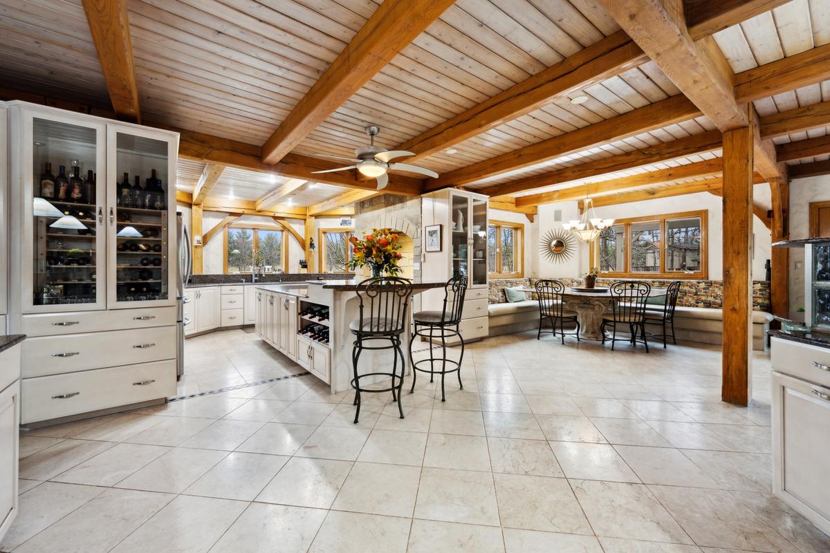 Heavy wooden beams accent the expert material science that went into designing every facet of this impressive home. Here you see the natural flow from the culinary space, to dining options, continuing into the welcoming living areas. (Baird & Warner)