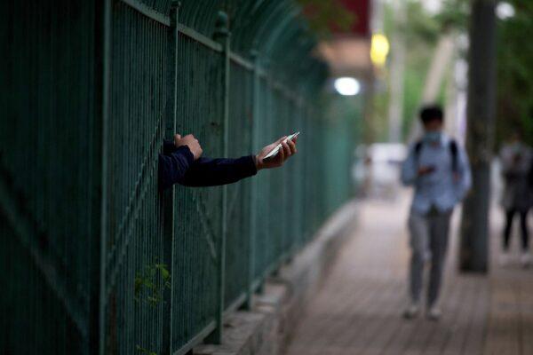 A resident holding a cellphone reaches out through a fence at a residential area under lockdown in the Panjiayuan Chaoyang district of Beijing on April 27, 2022. (Noel Celis/AFP via Getty Images)