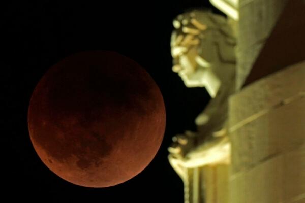 A lunar eclipse covers the moon as it rises beyond a statue atop the Liberty Memorial tower at the National World War I Museum in Kansas City, Mo., on May 16, 2022. (Charlie Riedel/AP Photo)