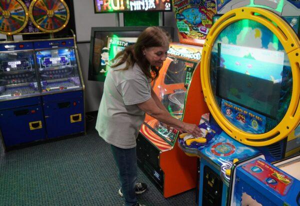 Mary Bacon, assistant manager of Jump City, a family recreation center, cleans an arcade machine in Imlay City, Mich., on May 13, 2022. (Steven Kovac/The Epoch Times)