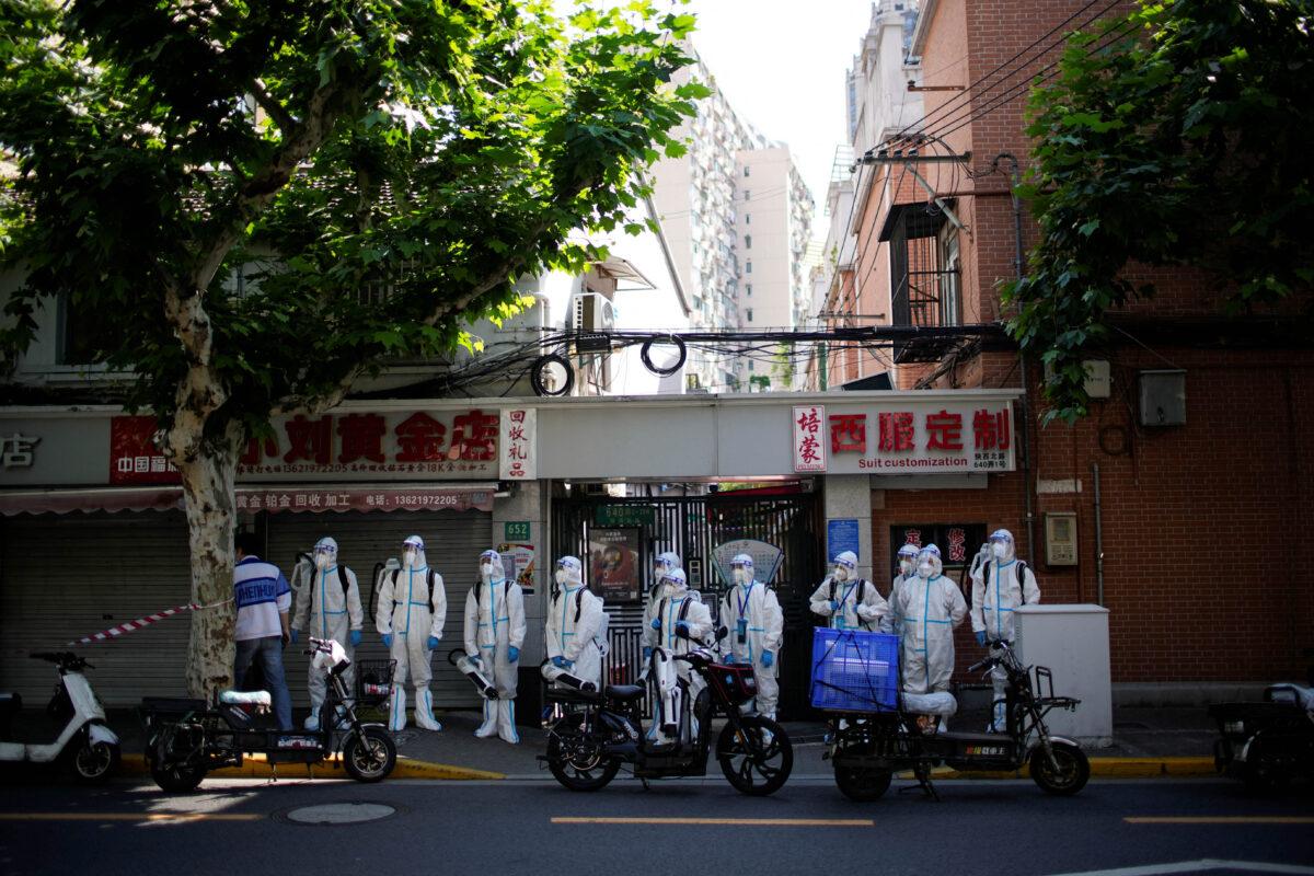 Workers in protective suits stand on a street as they disinfect during lockdown in Shanghai on May 18, 2022. (Aly Song/Reuters)