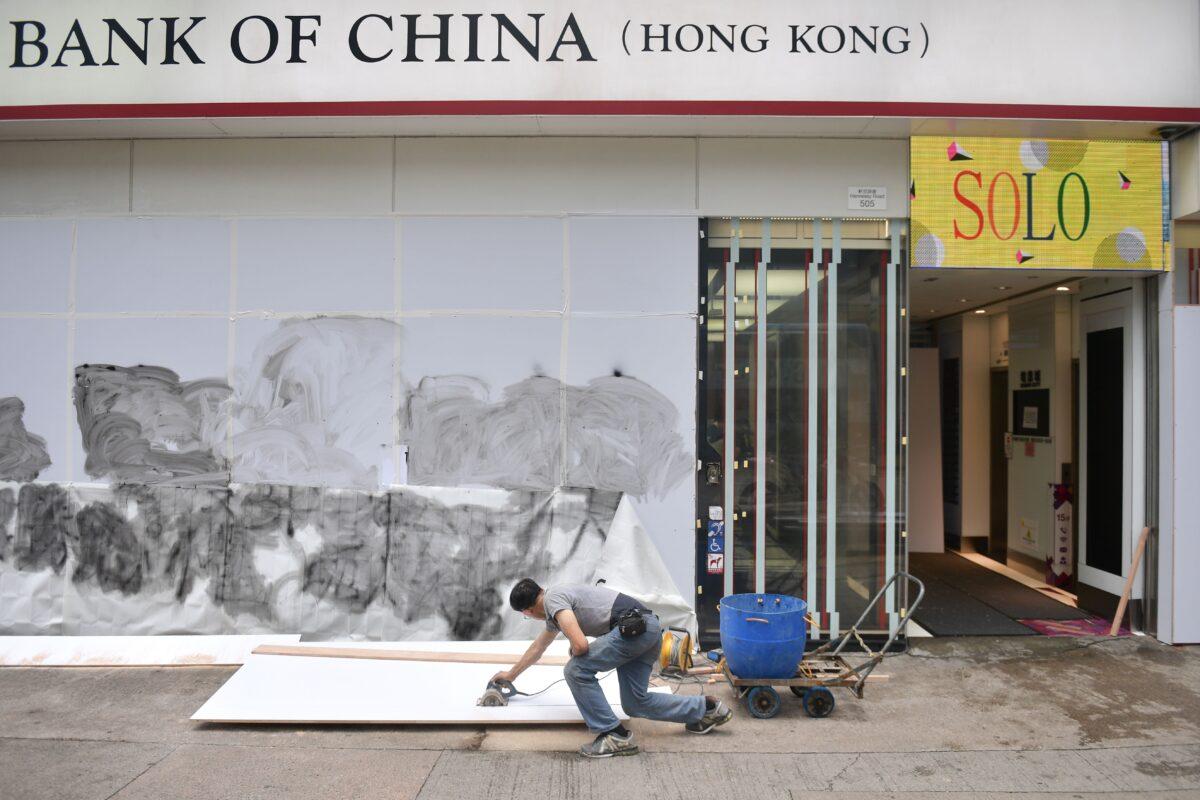 A worker cuts pieces of plywood to help cover up damage to a branch of the Bank of China after protesters smashed windows and vandalized the premises in the Causeway Bay shopping district in Hong Kong on Oct. 7, 2019. (Nicolas Asfouri/AFP via Getty Images)