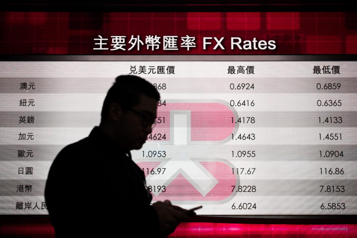 A man checks his mobile phone in front of an electronic board showing foreign exchange rates in Hong Kong on Jan. 20, 2016. (Phillipe Lopez/AFP via Getty Images)