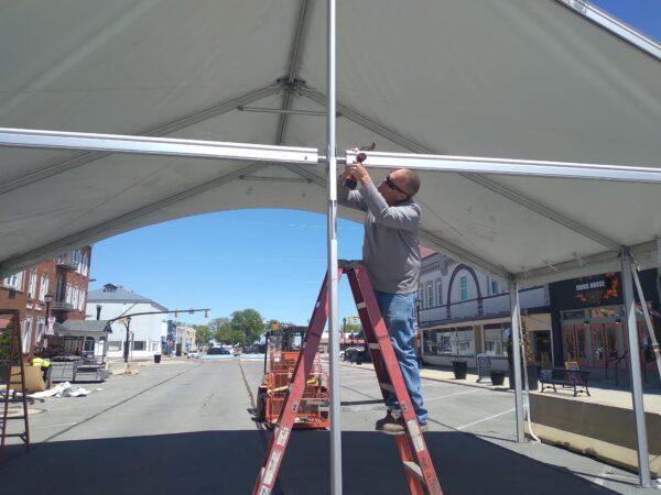 Gage Taylor tightens bolts on the tent on Madison Street where bands will play during its 41st Walleye Festival held May 26 through May 30 in Port Clinton, Ohio. The city of 6,000 is preparing for its tourist season while combating high fuel prices and supply chain issues. (Michael Sakal/The Epoch Times)