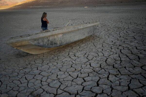Misha McBride looks at a formally sunken boat now on cracked earth hundreds of feet from what is now the shoreline on Lake Mead at the Lake Mead National Recreation Area, near Boulder City, Nev., on May 9, 2022. (John Locher/AP Photo)