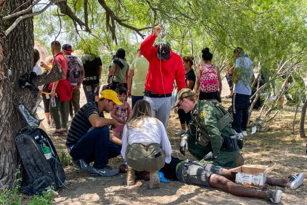 A Border Patrol agent provides medical assistance to an illegal immigrant who has heat-related issues, while other agents apprehend a large group of illegal immigrants near Eagle Pass, Texas, on May 20, 2022. (Charlotte Cuthbertson/The Epoch Times)