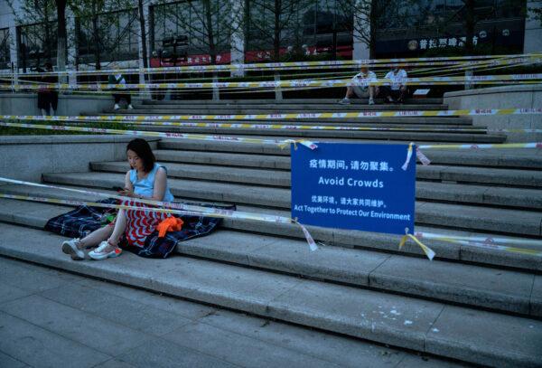 A woman sits on the steps behind tape and a sign placed by local police to prevent people from gathering in groups at a popular local park after recent COVID-19 outbreaks in Beijing on May 16, 2022. (Kevin Frayer/Getty Images)