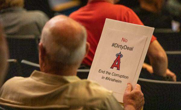 A man sits in on an Anaheim City council meeting session while holding a sign expressing against Anaheim's pending Angels Stadium deal in Anaheim, Calif., on May 24, 2022. (John Fredricks/The Epoch Times)