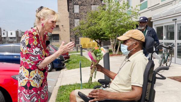 Patricia Gallagher (L) gives donated flowers to a resident of Stephen Smith Towers senior apartment and talks with him, in Philadelphia, Pa., on May 20, 2022. (William Huang/The Epoch Times)