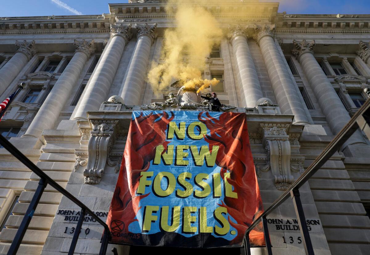 An environmental activist with the group Extinction Rebellion DC scales the Wilson Building next to a sign that reads "No New Fossil Fuels" as part of an Earth Day rally against fossil fuels in Washington on April 22, 2022. (Kevin Dietsch/Getty Images)