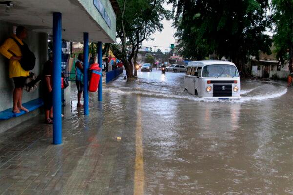 A woman stands on a bus stop bench as a driver of a Volkswagen van navigates a flooded street in Recife, state of Pernambuco, Brazil, on May 28, 2022. (Marlon Costa/Futura Press/AP Photo)