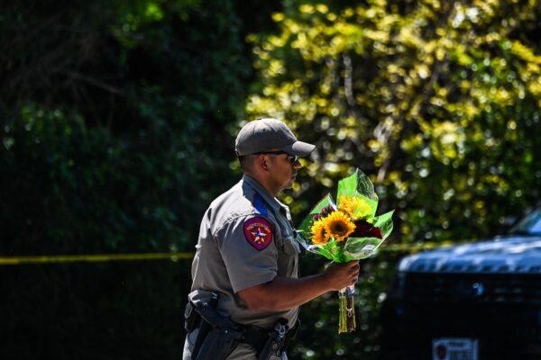 A police officer carries flowers at a makeshift memorial outside the Robb Elementary School in Uvalde, Texas on May 26, 2022. (Chandan Khanna/AFP via Getty Images)