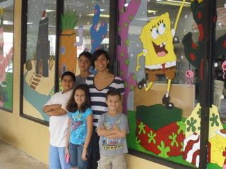 H.E.L.P. Miami high school graduate and artist posing with students in front of a Christmas mural they painted on school windows. (Courtesy of Barbara Rivera)