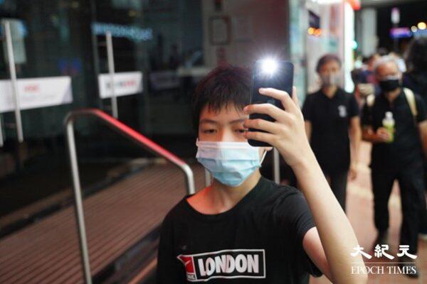 A little boy walking past the streets in Causeway Bay, raising a cell-phone above his head with light turned on. (Yu Gang/The Epoch Times, HK)