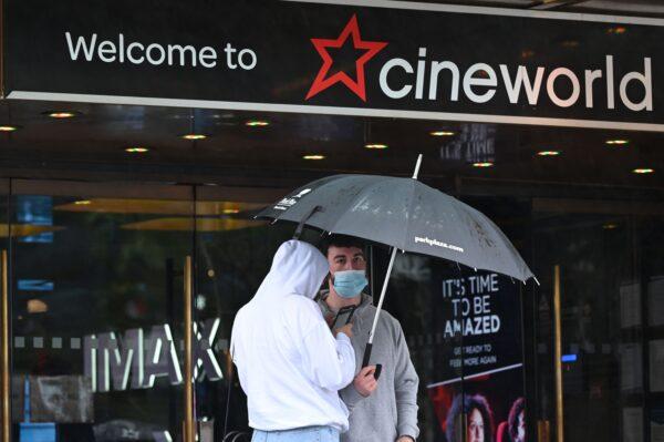 People shelter from the rain under an umbrella outside a Cineworld cinema in Leicester Square, London, on Oct. 4, 2020. (Justin Tallis/AFP via Getty Images)