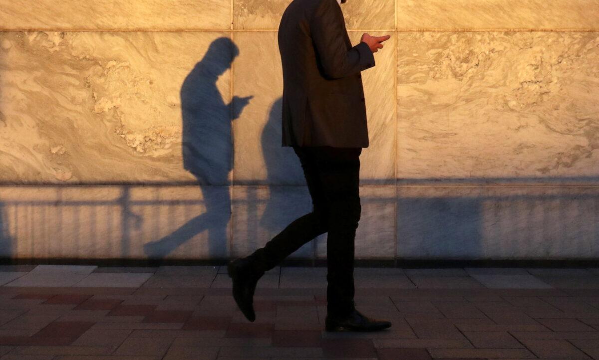 A man using a smartphone walks through London's Canary Wharf financial district in the evening light in London on Sept. 28, 2018. (Russell Boyce/Reuters)