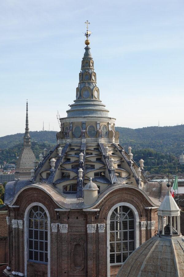 The Chapel of the Holy Shroud was added to the Royal Palace of Turin in the 17th century. Built by Italian architect Guarino Guarini, the complex dome is engineered with marble blocks that interlock in a self-supporting fashion. The multi-tiered tower was designed to include different geometrical forms that contrast at each level. An interlacing pattern of windows sits above smooth undulating arches with a spire rising above. A fire severely damaged the church in 1997, leading to a monumental restoration effort that took 28 years to complete. (Guilhem Vellut/CC BY 2.0)
