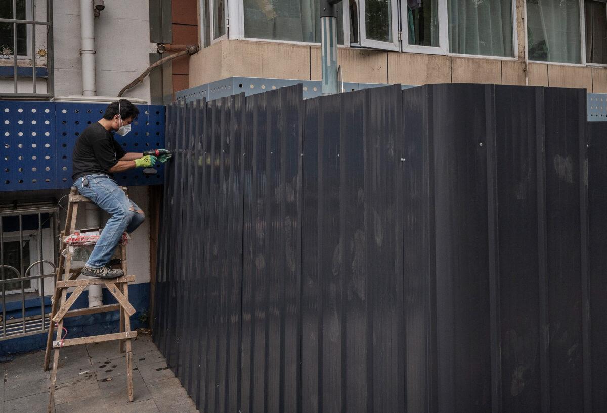 A worker drills a sheet into place on a barrier fence as he installs it outside an apartment that was locked down after a recent COVID-19 outbreak in Beijing on June 13, 2022. (Kevin Frayer/Getty Images)