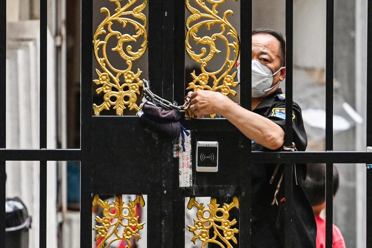 A security worker locks a door with a chain in a neighborhood under a COVID-19 lockdown in the Jing'an district of Shanghai on June 2, 2022. (Hector Retamal/AFP via Getty Images)
