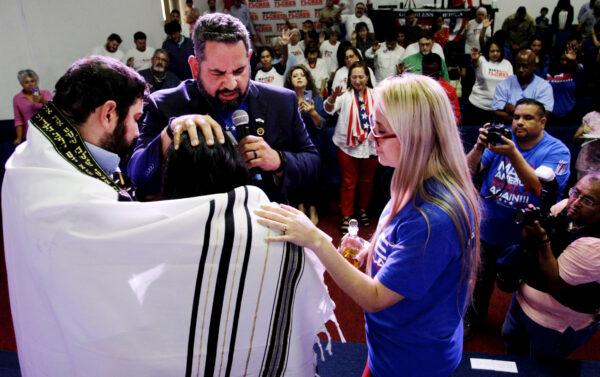 Pastor Luis Cabrera gives a special blessing to Mayra Flores (C), and her husband (L) using a Tallit, a Jewish prayer shawl, during a get-out-the-vote rally at City Church Harlingen. (Bobby Sanchez/The Epoch Times)