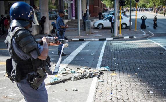 A riot police officers points his shot gun at protesters during clashes in October 2016 in Johannesburg. In July 2021 July, mobs rampaged across several South African cities, destroying property, looting stores and private homes, and attacking people. (Mujahid Safodien/AFP via Getty Images)